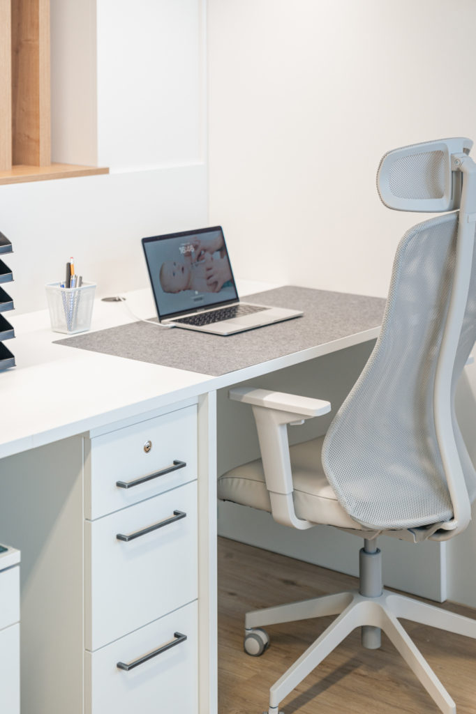Moderne Büroeinrichtung vom Tischler mit weißem Schreibtisch, ergonomischem Stuhl und Laptop